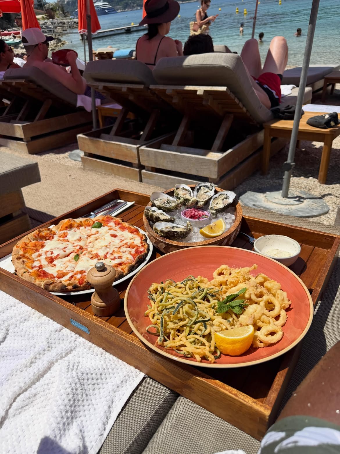 Pizza, oysters and fried calamari on a tray at a beach club