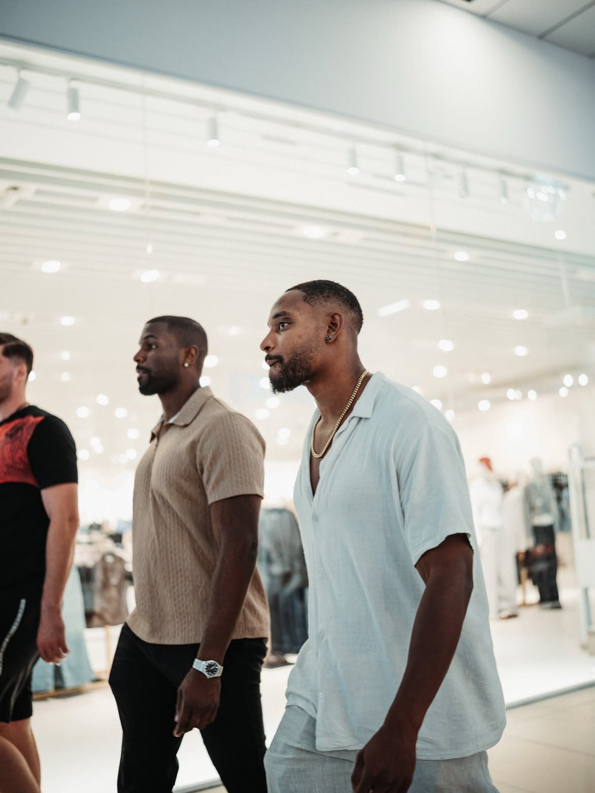 Martel walking through a bright shopping centre with two friends
